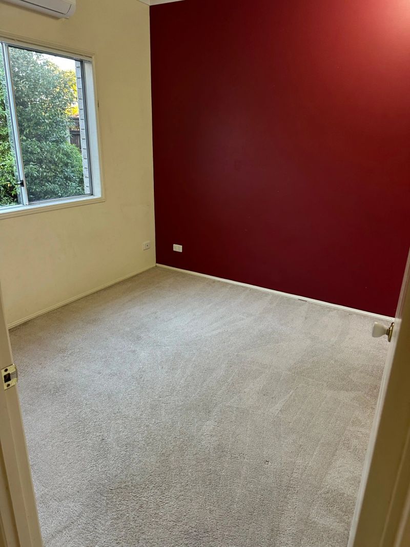 A clean, empty room with light-colored carpet and a red accent wall, demonstrating the results of carpet cleaning services.