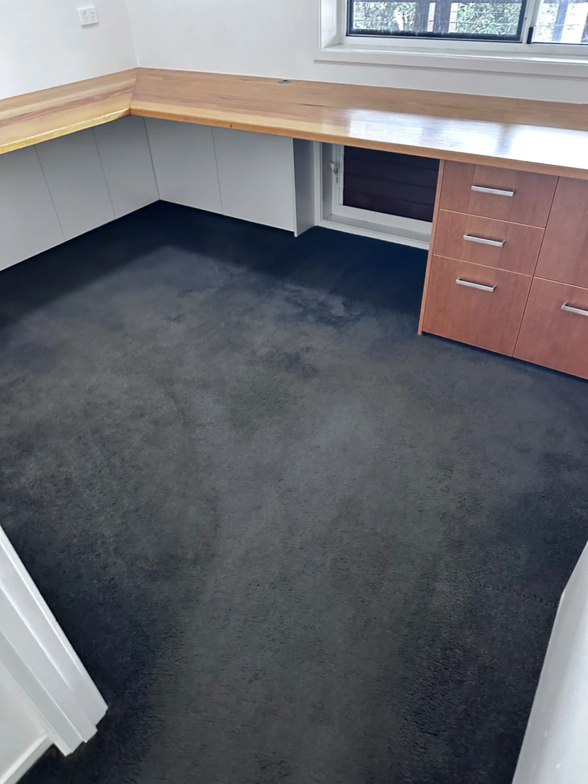 Clean office carpet with a wooden desk and drawers, showcasing a tidy workspace.