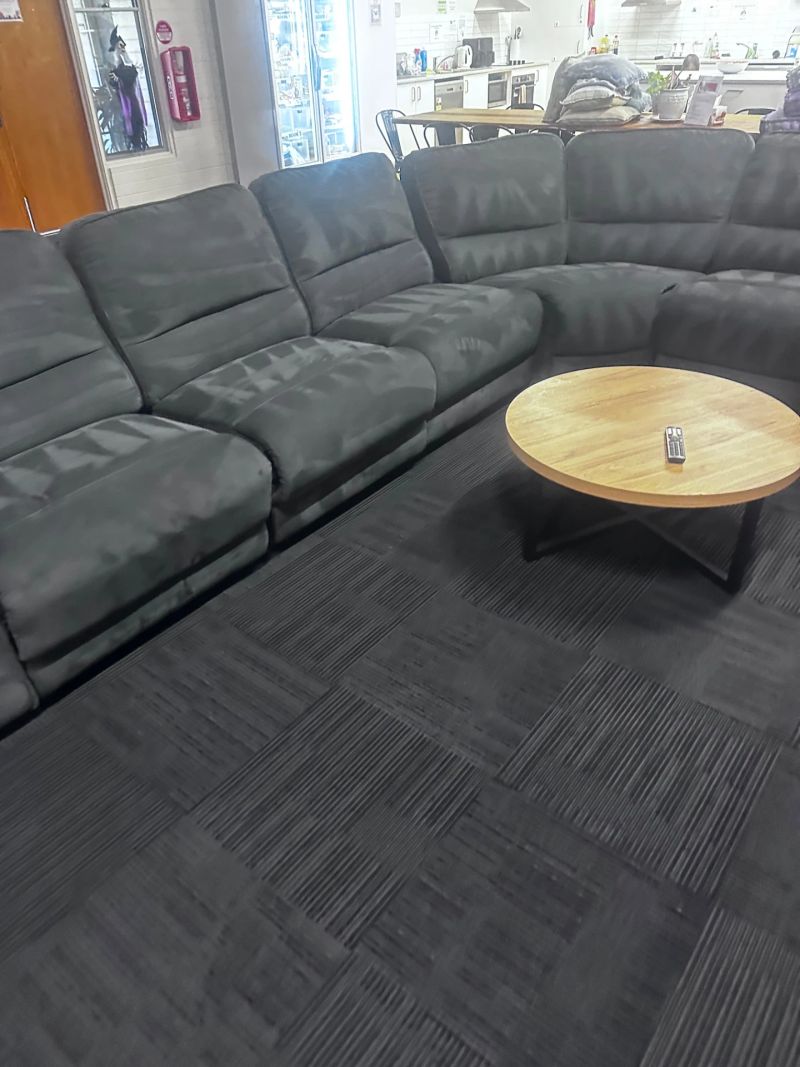 A large, comfortable dark grey sectional couch with a wooden coffee table in a spacious lounge area.